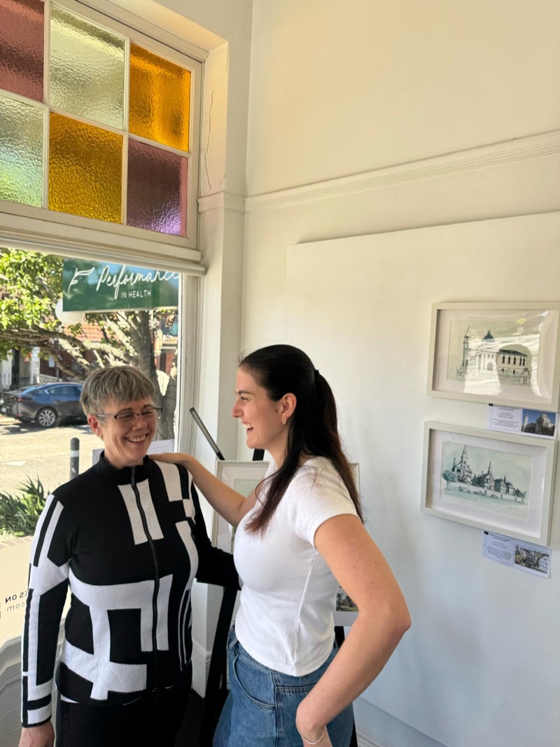 Lucy laughing with a student beside framed artwork in the studio