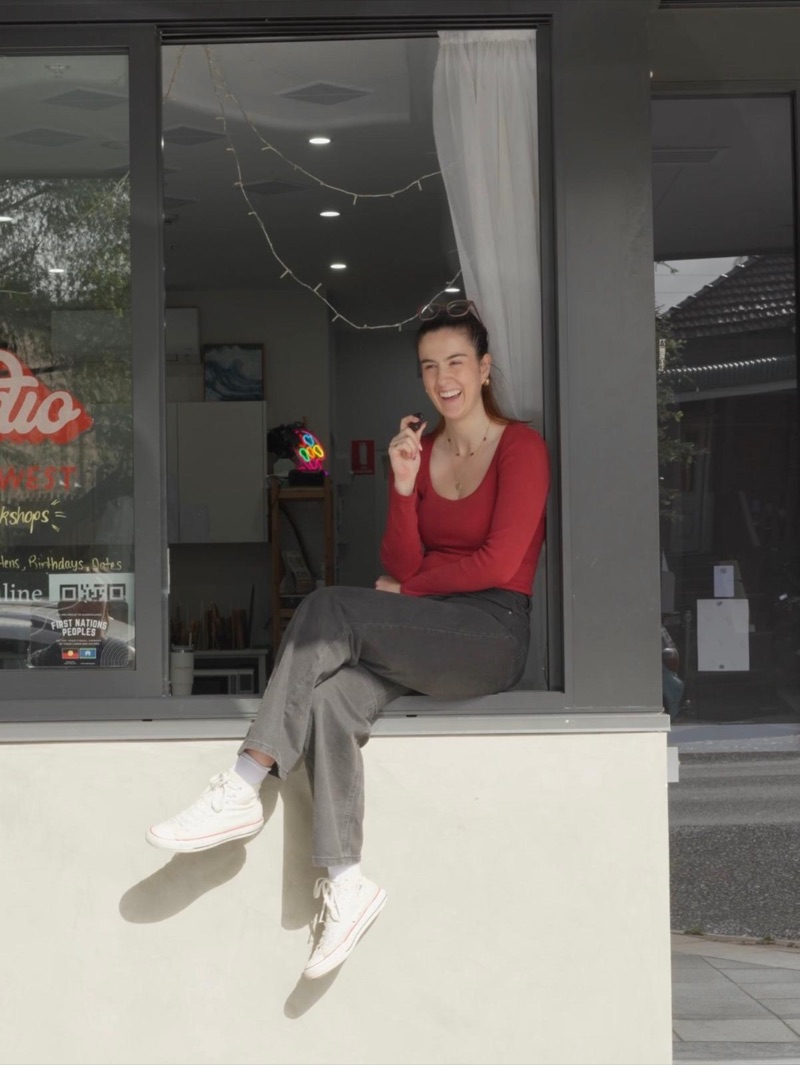Lucy Dujmovich laughing, seated in the front window of her Studio Inner West storefront
