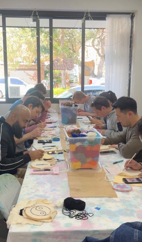 A full table of men learning punch needle at one of Lucy's workshops