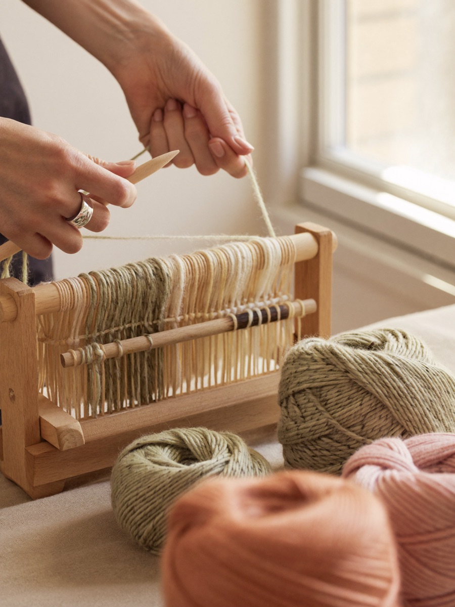 Hands weaving wool threads on a small frame loom